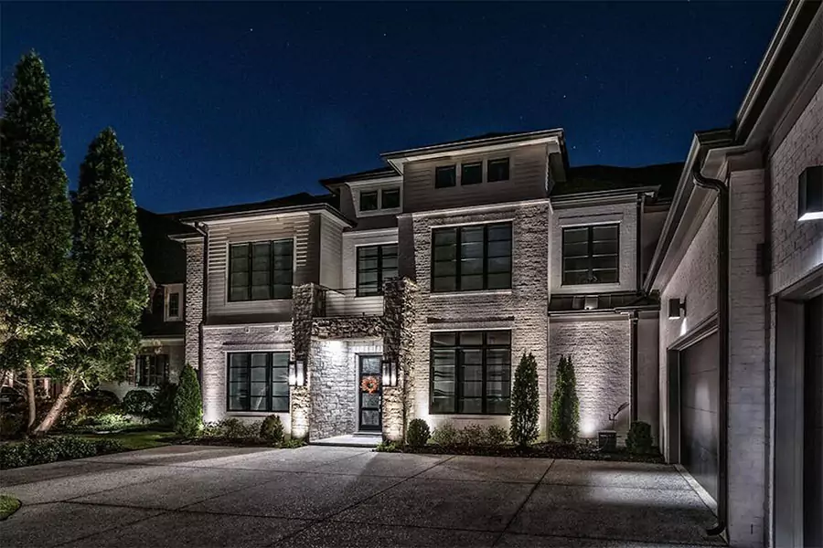 Luxury home exterior with architectural outdoor lighting highlighting stone columns and entryway at night.