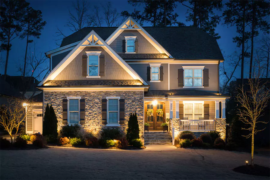 Two-story house with outdoor lighting highlighting stone facade and landscaping at dusk.