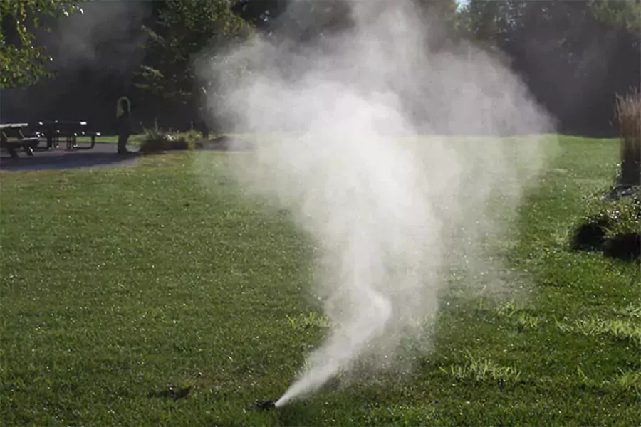Sprinkler system releasing mist during lawn irrigation in Indianapolis – importance of winterizing irrigation systems to prevent pipe damage.