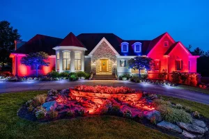 House at night with red, white, and blue landscape lighting highlighting the front yard and entryway.