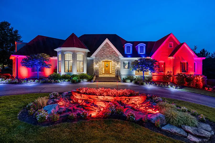 House at night with red, white, and blue landscape lighting highlighting the front yard and entryway.