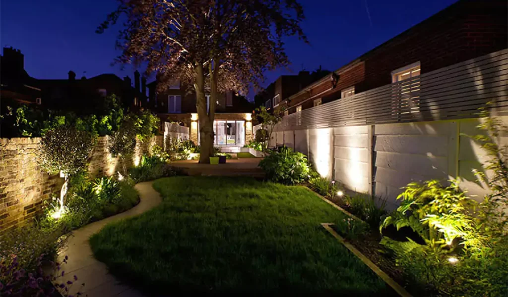 Well-lit backyard garden at night with landscape lighting and modern fencing, showcasing outdoor lighting setup in Indianapolis, IN