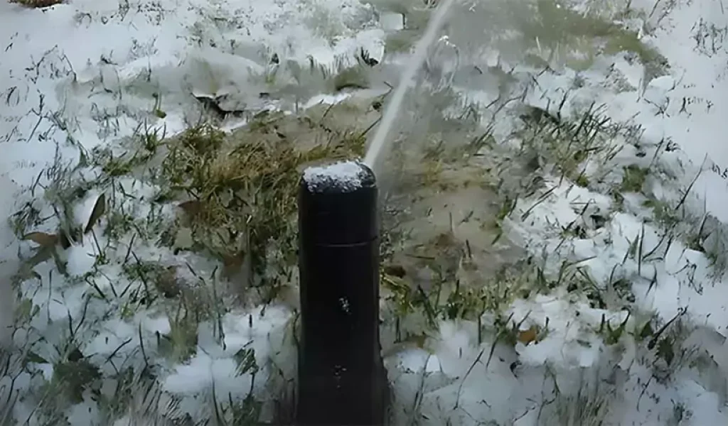 Frozen sprinkler head spraying water in a snowy yard in Indianapolis, IN.