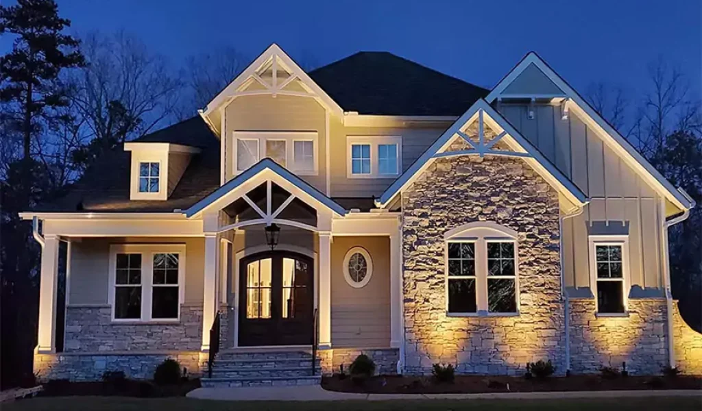 Beautiful two-story suburban home with stone facade and warm outdoor lighting illuminating the exterior at dusk.